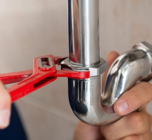 Plumber using a red wrench to tighten a shiny chrome pipe fitting.