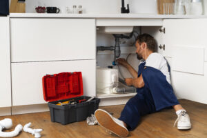 Plumber fixing pipes under a kitchen sink with tools and an open toolbox.